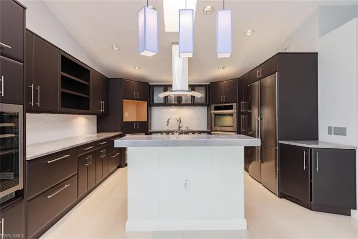 Kitchen featuring backsplash, island exhaust hood, pendant lighting, dark brown cabinets, and appliances with stainless steel finishes