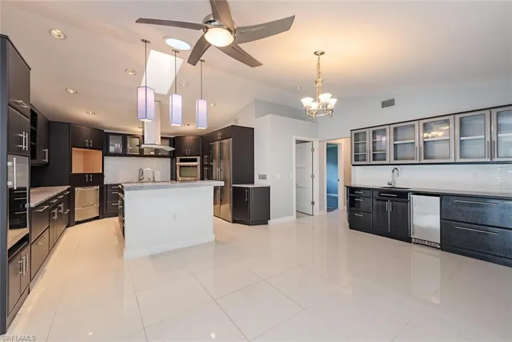 Kitchen featuring a center island with sink, decorative light fixtures, decorative backsplash, and vaulted ceiling