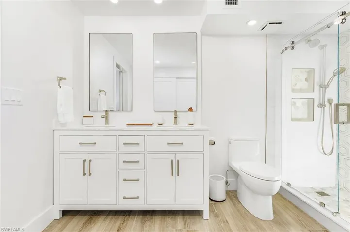 Bathroom featuring dual sinks, vanity with extensive cabinet space, a shower with door, hardwood / wood-style flooring, and toilet