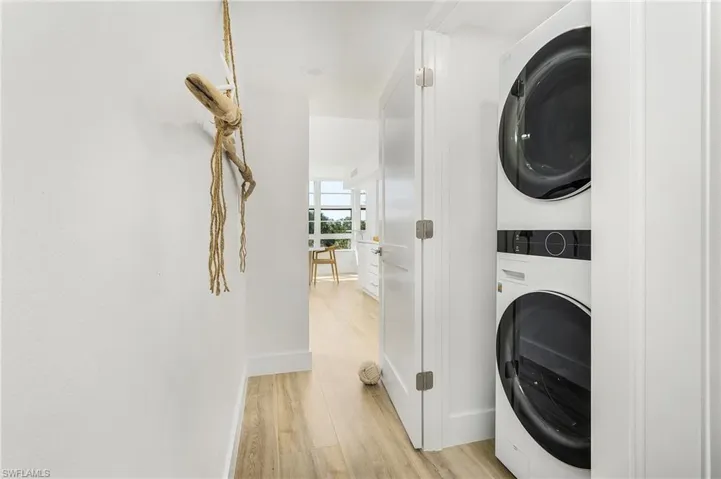 Washroom with stacked washing maching and dryer and light hardwood / wood-style floors