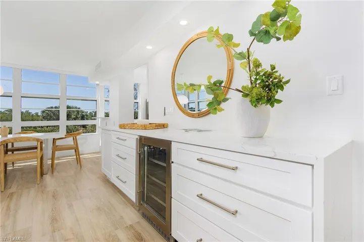 Kitchen featuring light hardwood / wood-style floors, light stone countertops, white cabinetry, beverage cooler, and ornate columns