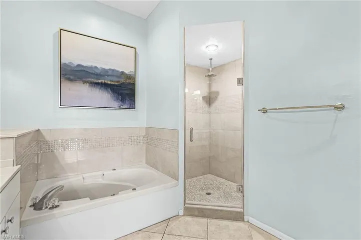 Corner soaking tub with tiled surround, glass-enclosed shower with tiled walls and pebble flooring, and light-toned tile flooring