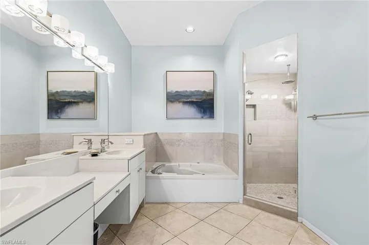 Dual vanity with white cabinetry and integrated sinks, a built-in soaking tub, and a glass-enclosed shower with tile surround and rain showerhead
