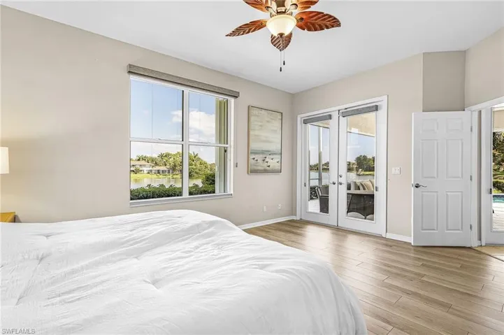 Wood-finish plank flooring, ceiling fan with light fixture, large window with roller shade, and double glass doors opening to outdoor living space