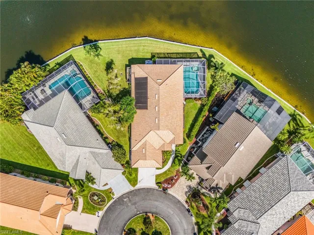 Waterfront property featuring a screened-in swimming pool, solar panels, a circular driveway, and mature landscaping