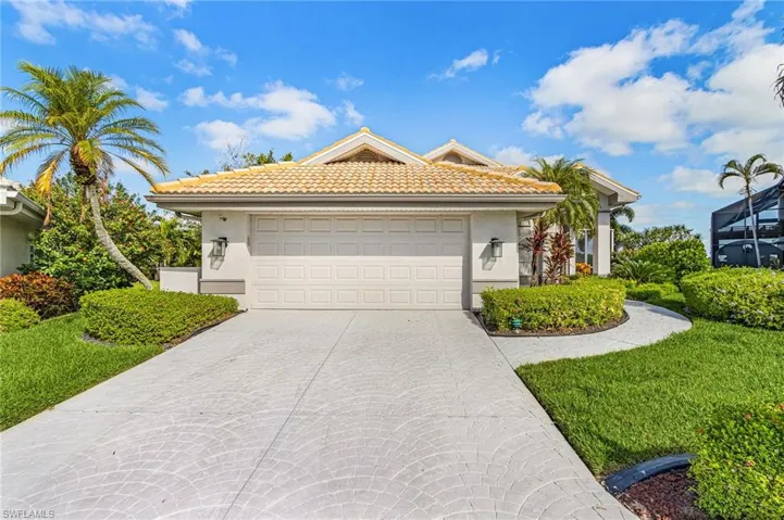 Textured concrete driveway, attached two-car garage, mature landscaping, tiled roof, and exterior wall sconces