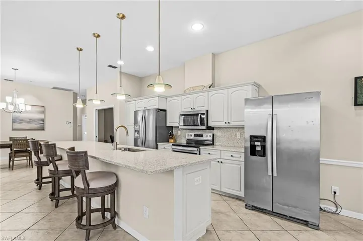 Kitchen featuring light-toned cabinetry, stainless steel appliances, a large center island with a sink, and pendant lighting