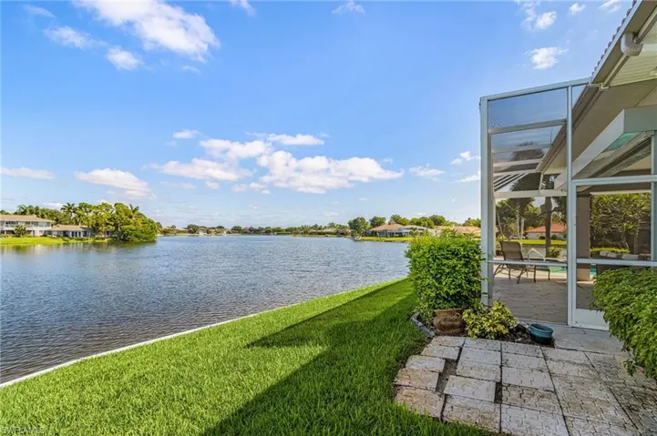 Expansive waterfront with a manicured lawn, screened patio, and stone paver pathway