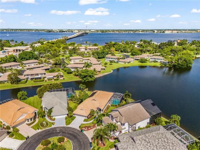 Waterfront property featuring a private screened pool enclosure, mature landscaping, and a circular driveway