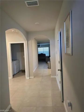 Hallway with arched walkways, light tile patterned flooring, and independent washer and dryer