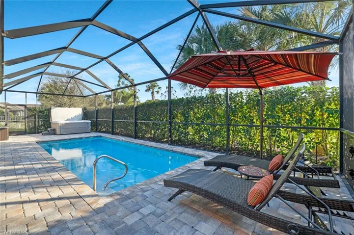 View of pool with a hot tub, glass enclosure, and a patio area