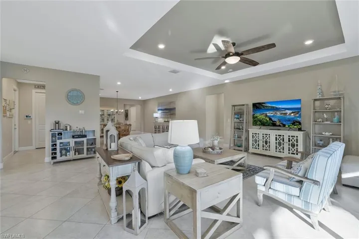 Tiled living room featuring a tray ceiling and ceiling fan with notable chandelier