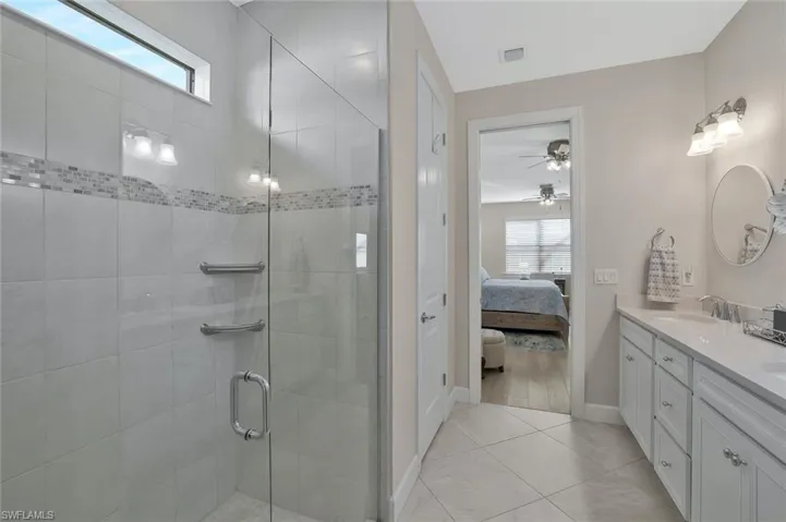 Bathroom featuring ceiling fan, vanity, tile patterned flooring, and a shower with door