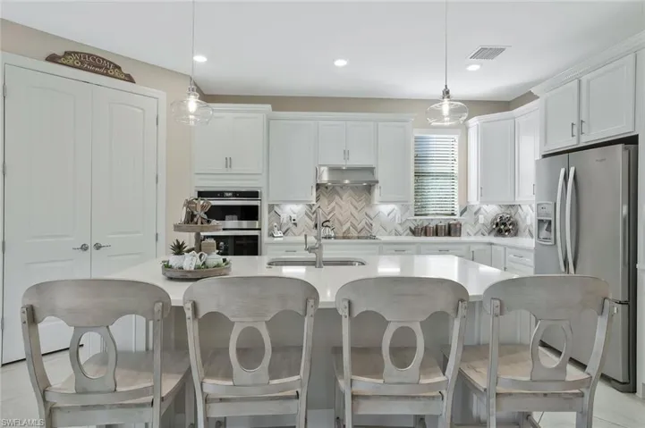 Kitchen with a kitchen island with sink, decorative light fixtures, white cabinets, and appliances with stainless steel finishes