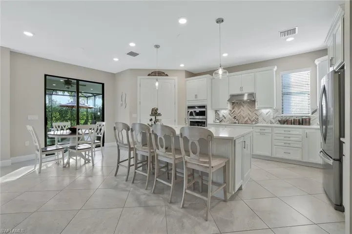 Kitchen featuring appliances with stainless steel finishes, hanging light fixtures, a kitchen breakfast bar, an island with sink, and white cabinets