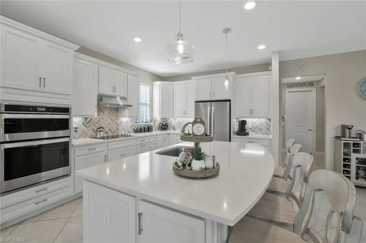 Kitchen with pendant lighting, white cabinetry, sink, stainless steel appliances, and a center island with sink