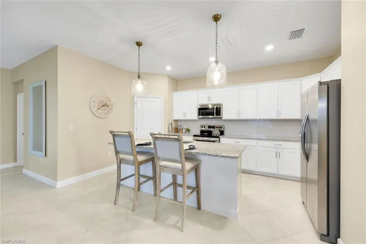Kitchen with white cabinets, light stone countertops, stainless steel appliances, an island with sink, and pendant lighting
