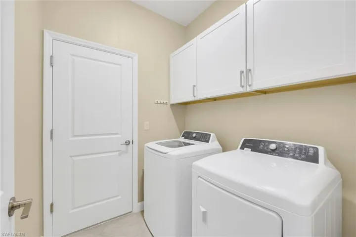 Laundry room featuring light tile patterned floors, washing machine and clothes dryer, and cabinets