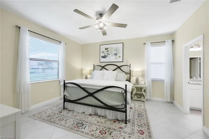 Bedroom with light tile patterned flooring, connected bathroom, and ceiling fan