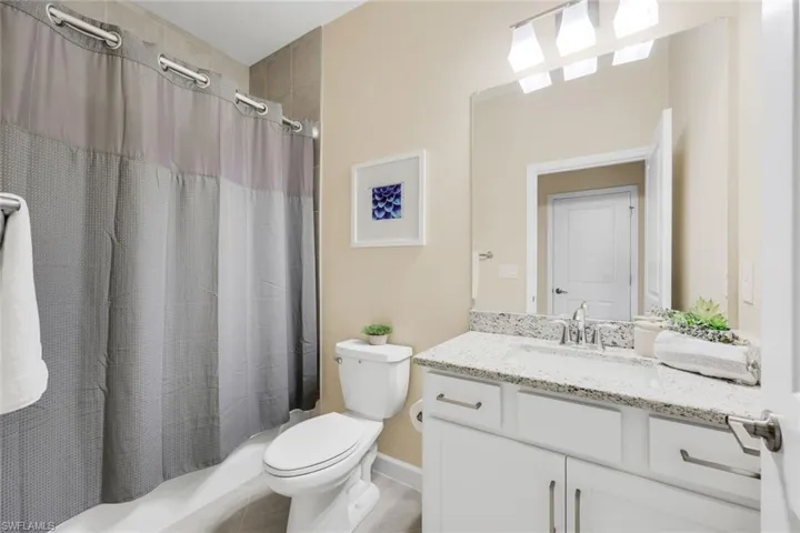 Full bathroom with tile patterned floors, shower / bathtub combination with curtain, toilet, and vanity