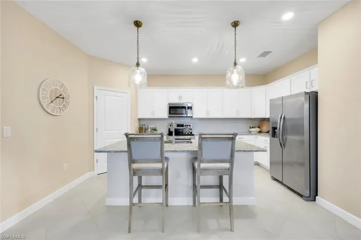 Kitchen featuring an island with sink, stainless steel appliances, light stone countertops, and tasteful backsplash