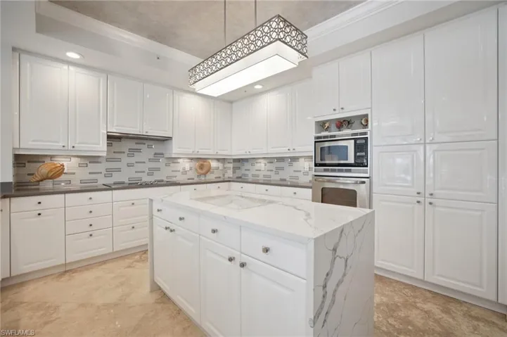 Kitchen with white cabinets, a kitchen island, appliances with stainless steel finishes, dark stone countertops, and ornamental molding