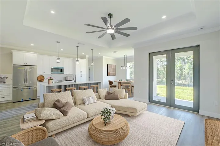 Virtual Stage - Living room featuring a raised ceiling, light wood-type flooring, ornamental molding, a ceiling fan, and french doors