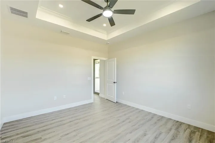 Empty room with a tray ceiling, light wood-type flooring, crown molding, and recessed lighting