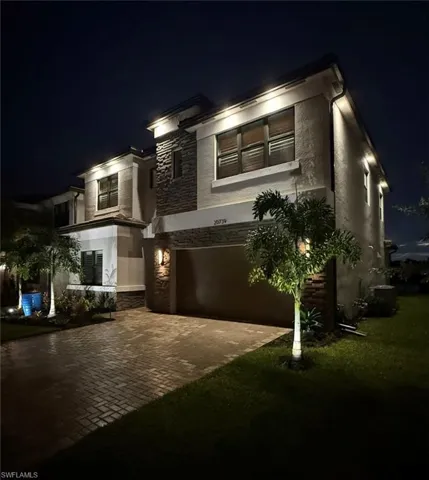 Modern home featuring stone siding, a garage, decorative driveway, and stucco siding