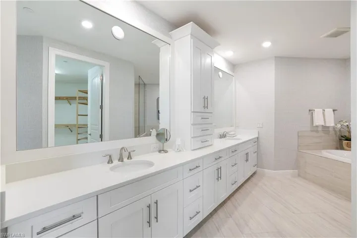 Bathroom with double vanity, a spacious closet, and a garden tub