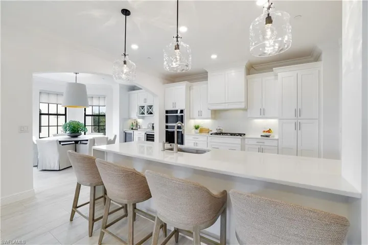 Kitchen featuring a breakfast bar, white cabinets, arched walkways, decorative light fixtures, and ornamental molding