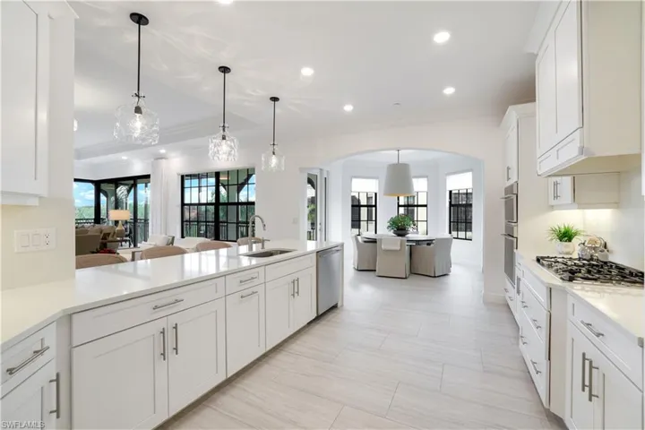 Kitchen featuring white cabinets, light stone counters, a peninsula, hanging light fixtures, and ornamental molding
