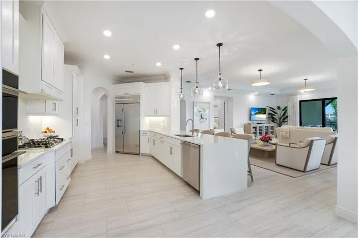 Kitchen featuring arched walkways, white cabinetry, light stone counters, a peninsula, and a breakfast bar