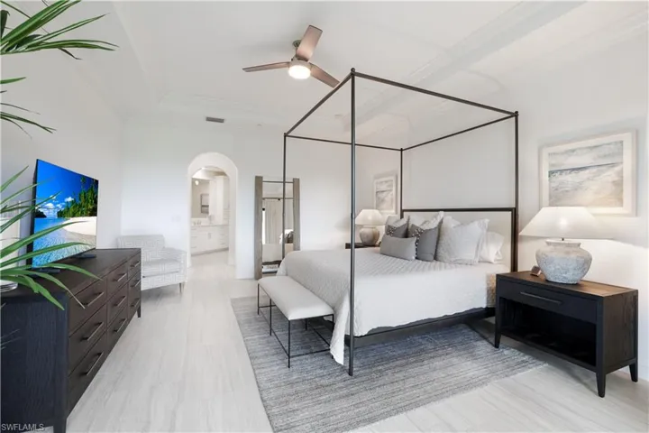 Bedroom with arched walkways, a ceiling fan, ornamental molding, and ensuite bath