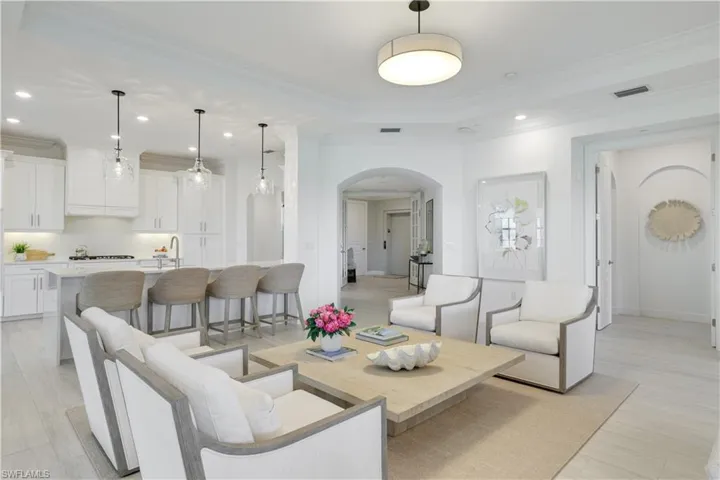 Living room featuring arched walkways, crown molding, recessed lighting, a tray ceiling, and light wood-style flooring