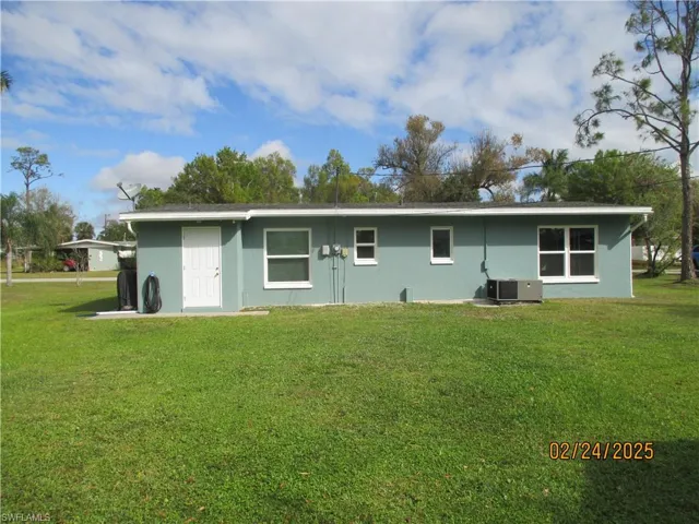 Rear view of house with stucco siding, central AC unit, and a yard