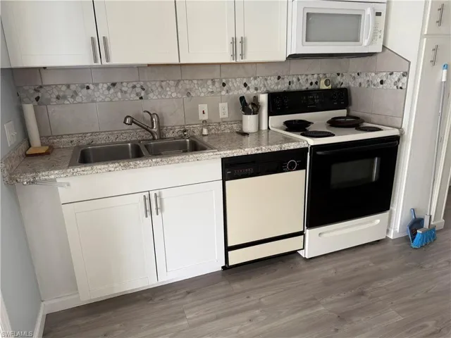 Kitchen featuring decorative backsplash, white appliances, sink, wood-type flooring, and white cabinetry