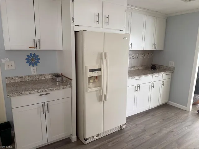 Kitchen with white cabinets, light stone counters, and white fridge with ice dispenser
