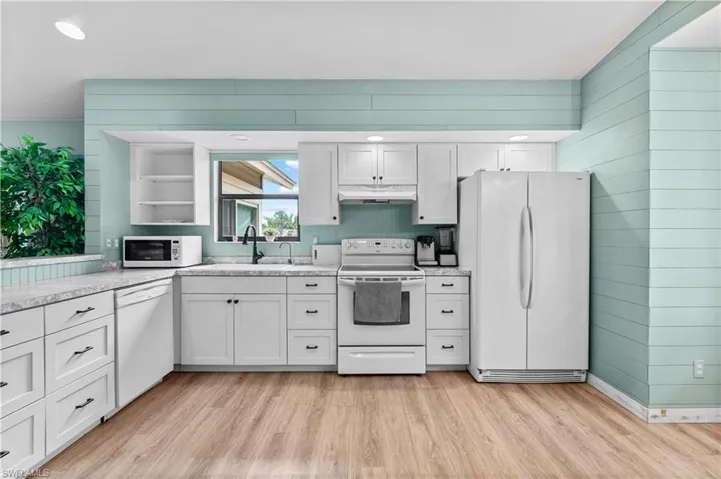 Kitchen with white appliances, open shelves, light wood-type flooring, wood walls, and under cabinet range hood