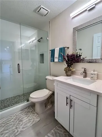 Full bath with a shower stall, vanity, a textured ceiling, and dark wood finished floors