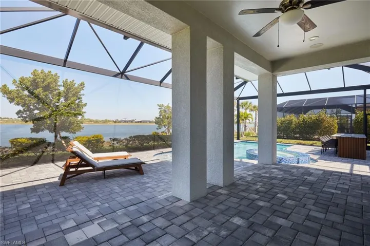 View of patio / terrace featuring a water view, outdoor dining space, a pool with connected hot tub, glass enclosure, and ceiling fan