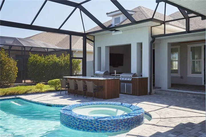 View of swimming pool featuring area for grilling, a pool with connected hot tub, outdoor wet bar, and a patio