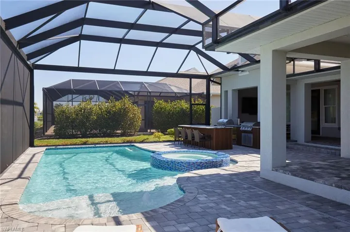 View of swimming pool with a pool with connected hot tub, a lanai, exterior kitchen, a patio area, and a grill