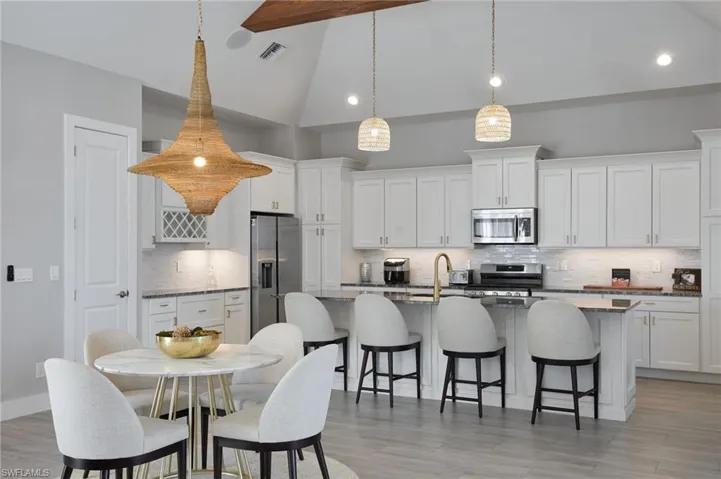 Kitchen with visible vents, high vaulted ceiling, a kitchen island with sink, stainless steel appliances, and a breakfast bar area