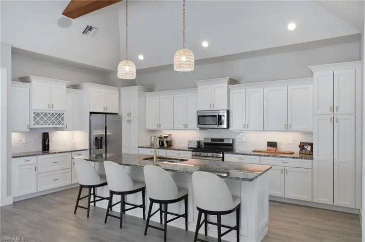Kitchen featuring visible vents, a kitchen bar, appliances with stainless steel finishes, white cabinets, and a sink