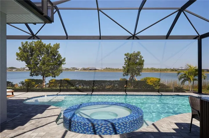 View of pool with a lanai, a water view, and a pool with connected hot tub
