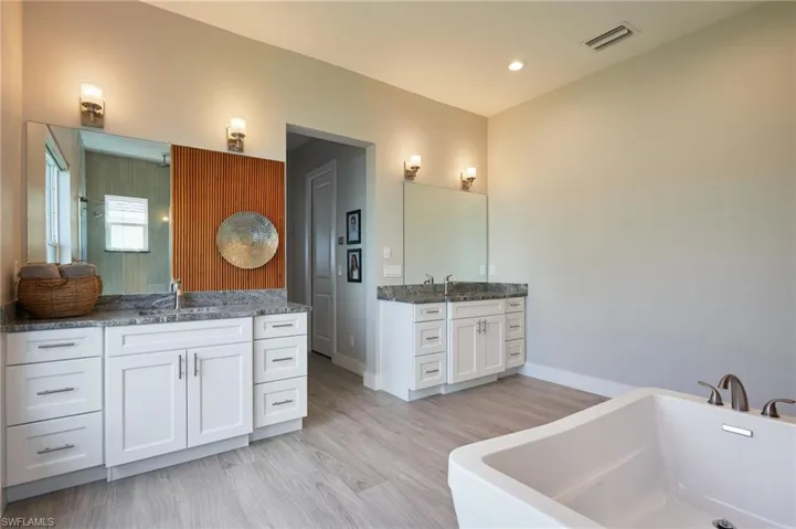 Full bath featuring a sink, visible vents, a soaking tub, and two vanities