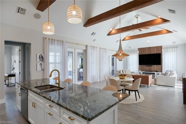 Kitchen featuring visible vents, beamed ceiling, a kitchen island with sink, a sink, and light wood finished floors