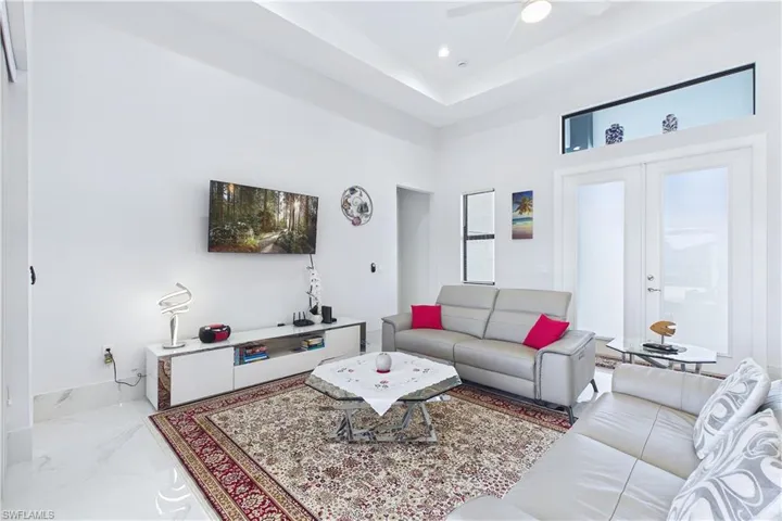 Living room featuring a raised ceiling, french doors, a ceiling fan, and recessed lighting