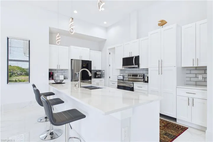 Kitchen featuring stainless steel appliances, backsplash, a breakfast bar, white cabinets, and light stone counters